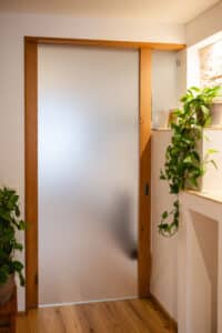 Ein Schiebetür‑Element mit elegantem Holzrahmen und satiniertem Glas, das Räume lichtdurchflutet und dennoch Privatsphäre wahrt aus der Tischlerei Scharnreitner.