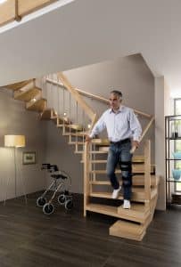 Ein Mann geht eine alters- und beeinträchtigungsgerechte Holztreppe mit zusätzlicher Halbstufe für besseren Treppenauftritt hinunter.