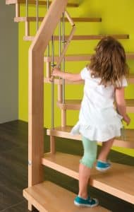Kleines Kind läuft eine Holztreppe mit zweitem Handlauf in kindgerechter Höhe hinauf.