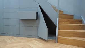 Futuristischer Treppenverbau mit Treppenschrank in Dunkelgrau, grifflosen Fronten und Schubladen und Stufen in hellem Holz.