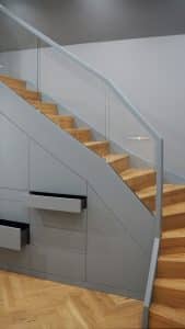 Futuristischer Treppenverbau mit Treppenschrank in Dunkelgrau, grifflosen Fronten und Schubladen und Stufen in hellem Holz.