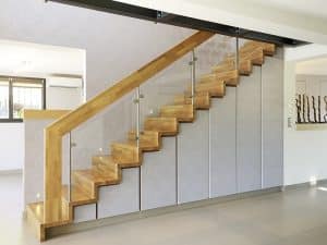 Treppenschrank mit tapezierten grifflosen Fronten und einer Holztreppe mit Geländer aus Holz, Eisen und Glas.
