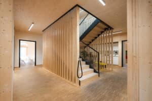 Ein großzügiger Holztreppen‑Aufgang mit Glasgeländer, eleganten Wänden aus Holzsprossen, Handlauf und Wangen in mattschwarzem Stahl von Treppenmeister.