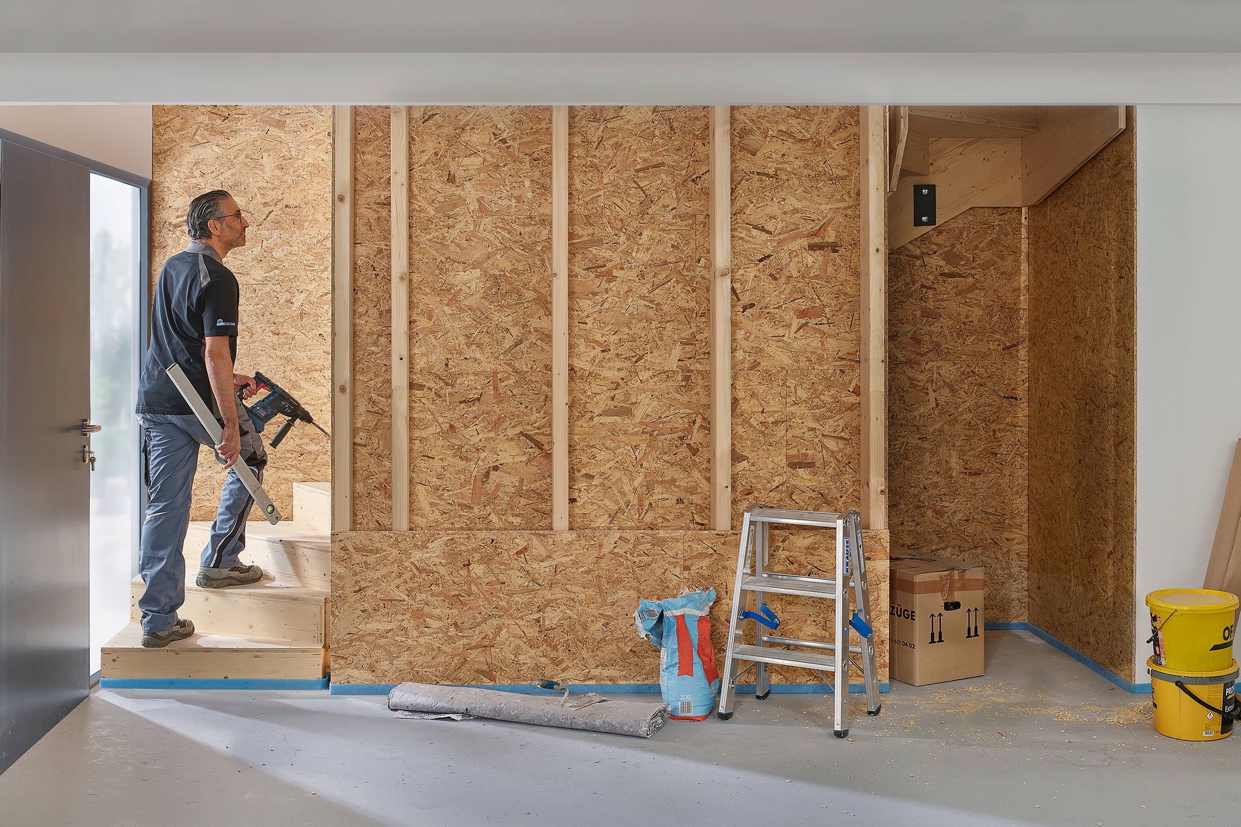 Ein Handwerker arbeitet an einer Treppe von Treppenmeister welche durch einen Wandverbau und die Integration des Untertreppenstauraums eine zusätzliche Abstellkammer bekommt.