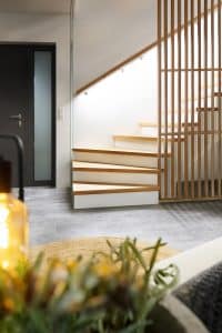Eine fertige Treppe mit beleuchtetem Holzhandlauf auf der einen, Holzsprossengeländer auf der anderen Seite, Stufen mit Holzauftritt und einer deckenhohen Glaswand am Treppenende von Treppenmeister.