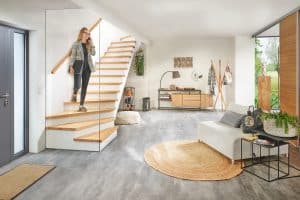 Eine Frau schreitet über ihre Treppe mit Holzhandlauf, Stufen mit Holzauftritt, freiem Untertreppenstauraum und einer deckenhohen Glaswand am Treppenende von Treppenmeister.