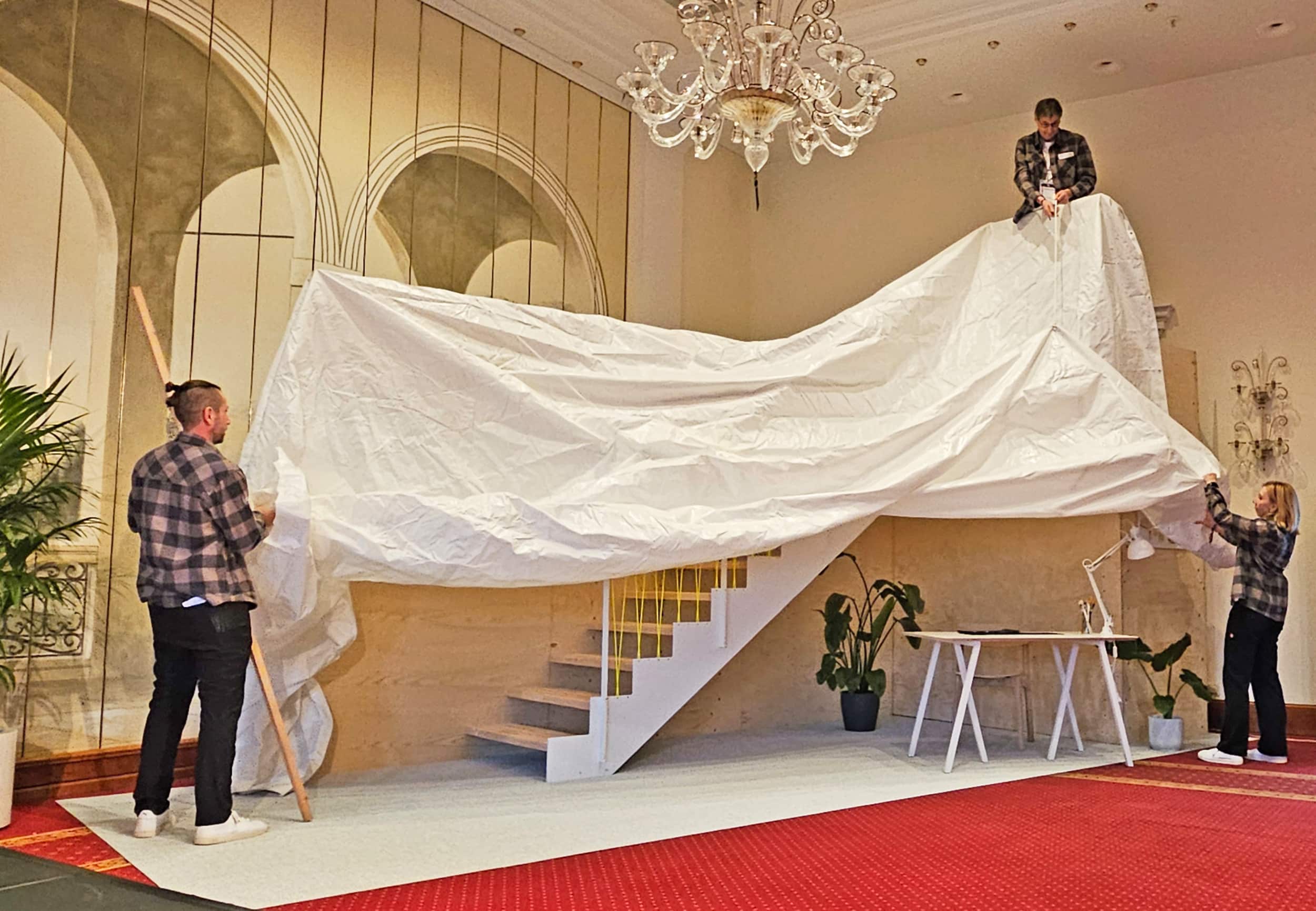 Die auf der Bühne aufgebaute Schautreppe von Treppenmeister wird von drei fleißigen Mitarbeitern enthüllt.