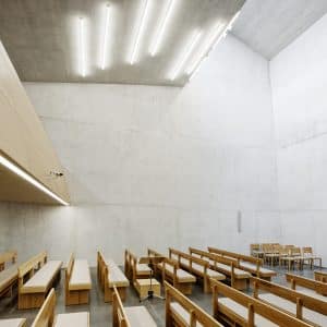 Kirchenraum der Neuapostolische Kirche in Wien Penzing mit Wänden und Decken aus Beton und Holzsitzbänken.