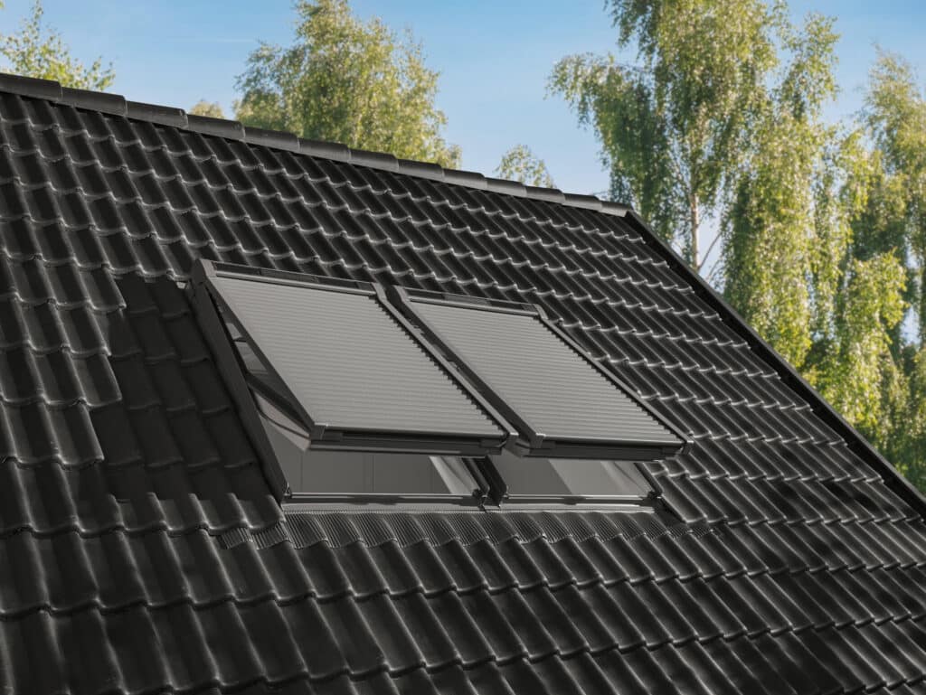 Velux zeigt zwei gekippte Dachfenster in einem Satteldach mit Rollladen-System, das unabhängig vom Fenster montiert ist und so optimal vor Sonneneinstrahlung schützt.