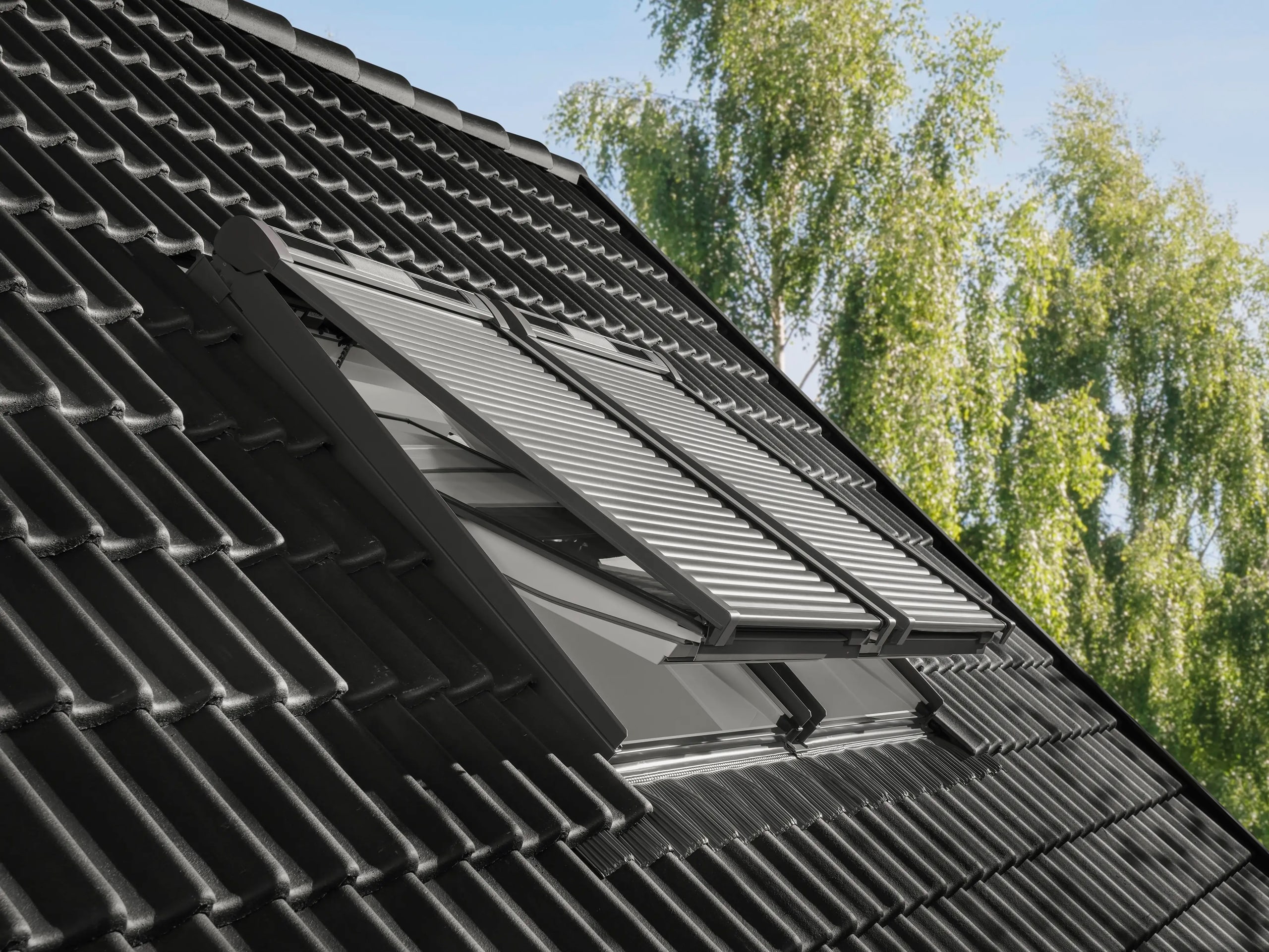 Velux zeigt zwei gekippte Dachfenster in einem Satteldach mit Rollladen-System, das unabhängig vom Fenster montiert ist und so optimal vor Sonneneinstrahlung schützt.