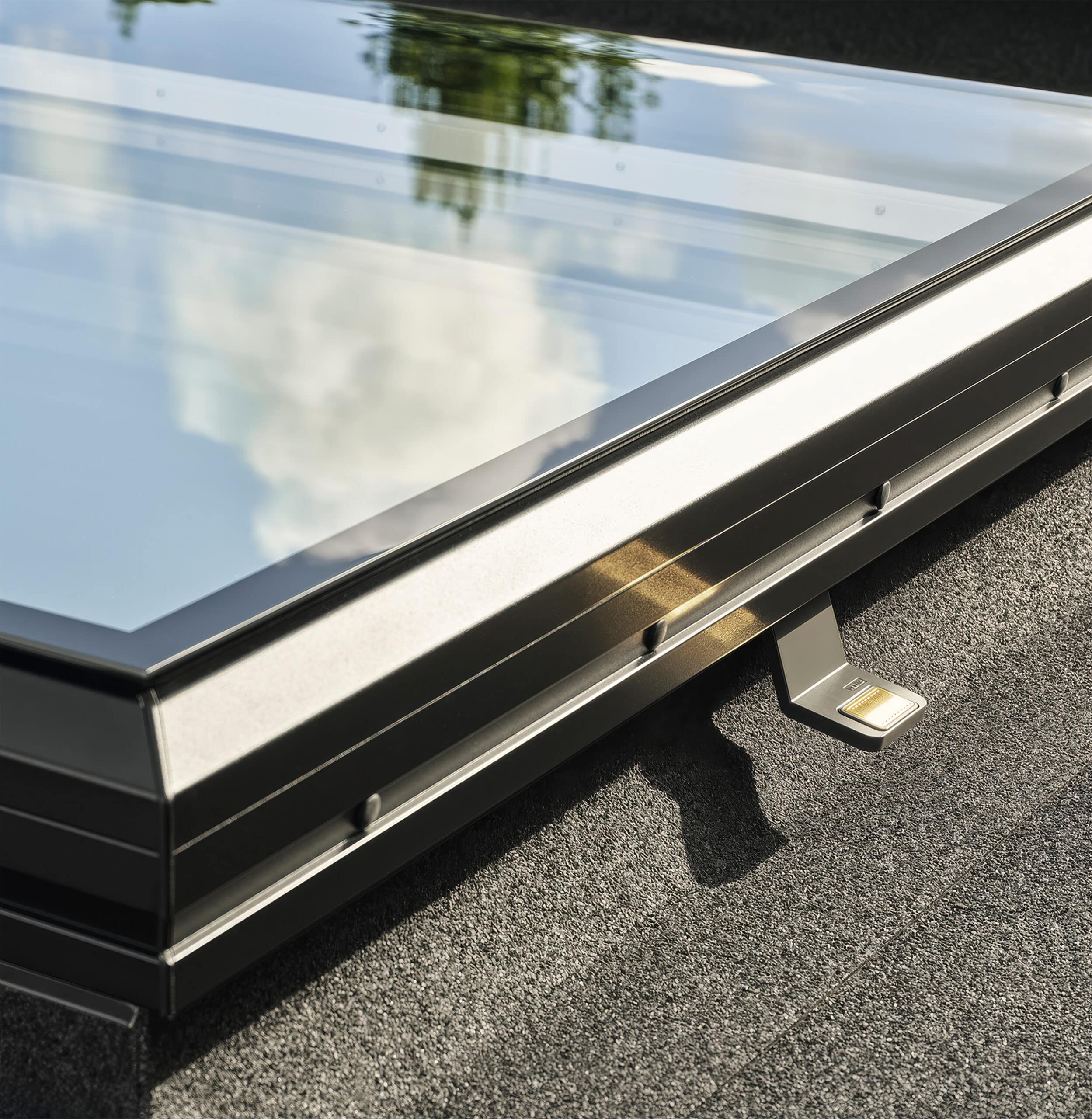 VELUX zeigt ein geschlossenes dunkelgraues Flachglasfenster mit Hebelmechanismus zum Öffnen in der Detailansicht auf einem Flachdach.