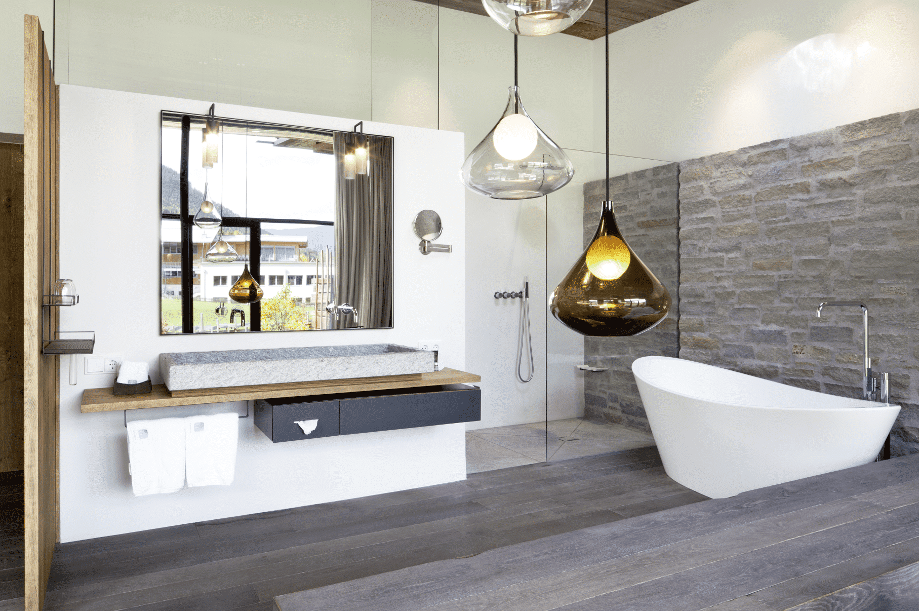 Badezimmer mit freistehender Wanne, Waschtisch mit Waschbecken aus Granit und Armaturen am Spiegel montiert von VOLA.