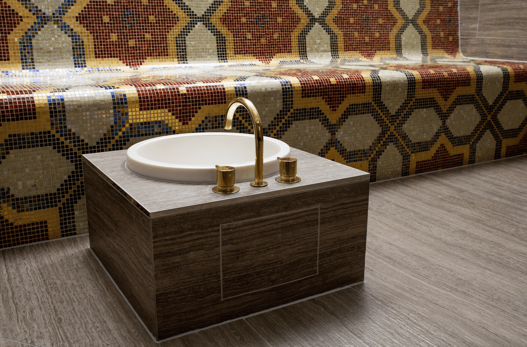 Gebogene Armatur in gold von VOLA über einem runden Waschbecken in einer Dampfsauna.