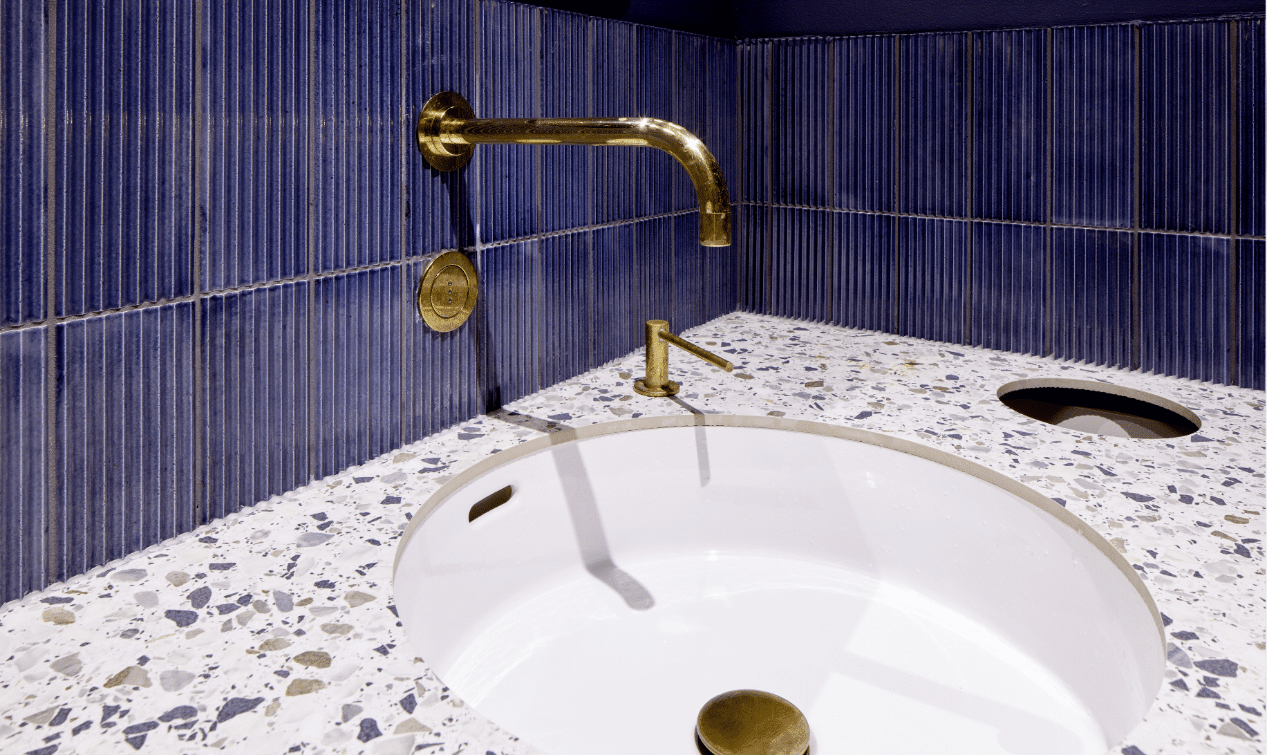 Elegante WC-Anlage mit blauen Wänden und goldenen Wandarmaturen und Seifenspendern von VOLA über flächenbündigen Waschbecken.