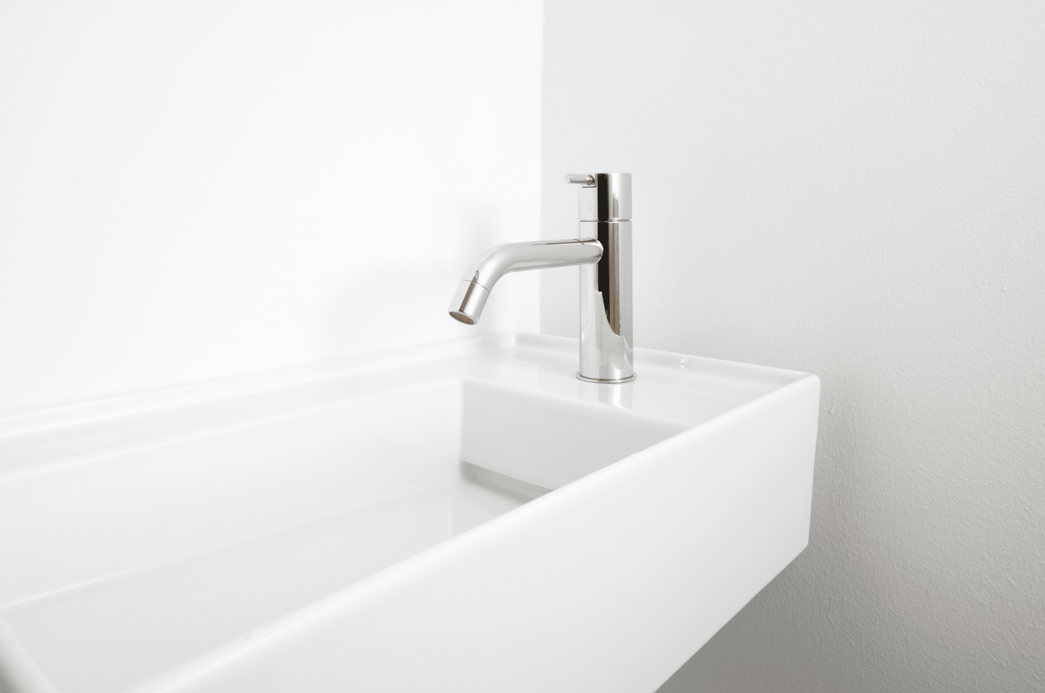 Schmales Waschbecken mit seitlich montierter Armaturen aus Chrom von VOLA.