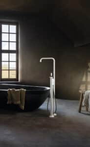 VOLA präsentiert ein Badezimmer mit freistehender schwarzer Badewanne und einem freistehendem Wassereinlauf mit Handbrause in Weiß.