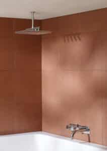 VOLA präsentiert eine Regendusche mit stabförmigen Düsen über einer Badewanne und einen Wanneneinlauf mit drei Reglern aus glänzendem Chrom.