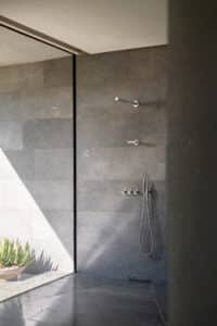 VOLA präsentiert eine Kombination von zwei stabförmigen Kopfduschen, einer Handdusche, drei Reglern und aus mattem Chrom an der Wand montiert.