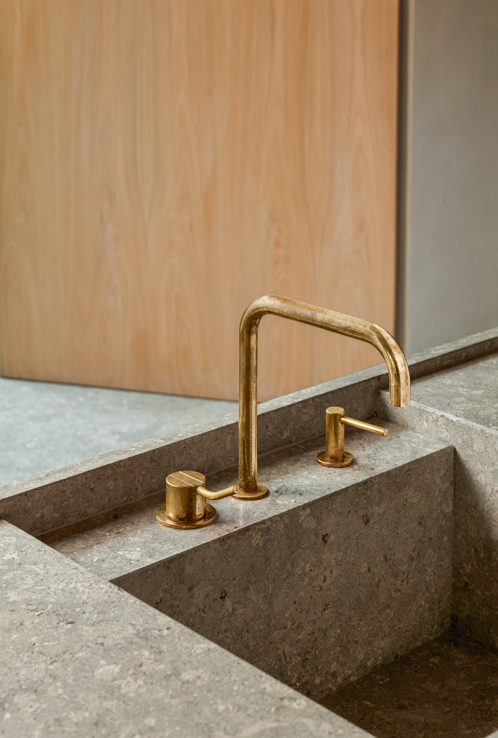 VOLA zeigt das Marmor-Spülbecken einer Küche mit Doppelschwenkauslauf und zweit Mischergriffen aus Messing.