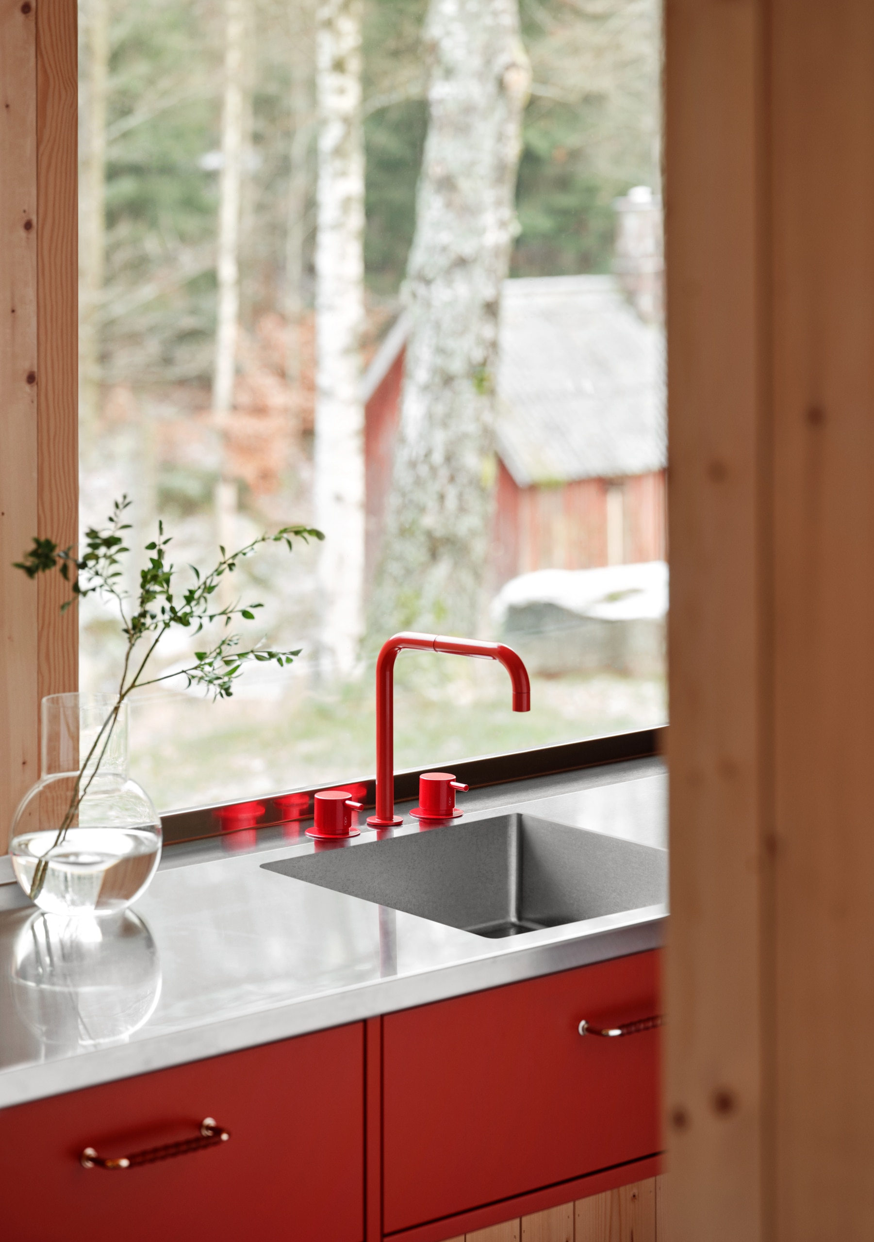 VOLA zeigt das Spülbecken einer hellen Küche mit rotem Wasserauslauf und zweit roten Mischergriffen.