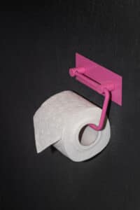 VOLA zeigt ein dunkel verfliestes WC mit rosa farbenem Klopapierhalter.