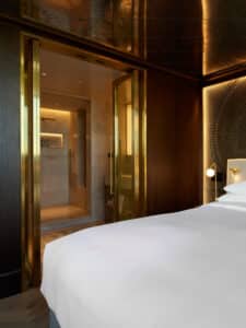 VOLA präsentiert ein elegantes Schlafzimmer in einem Hotelzimmer mit Blick in das Badezimmer mit Dusche und goldenen Armaturen.