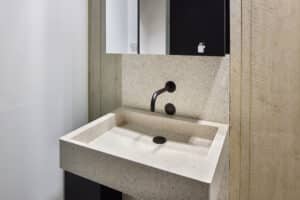 VOLA zeigt ein Waschbecken mit Armatur mit Sensor in schwarz, die in der Wand integriert ist und einer schwarzen Abflussabdeckung.