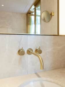 VOLA zeigt ein Marmor-Waschbecken eines Hotelzimmers mit Armaturen in gold, die in der Wand integriert sind.
