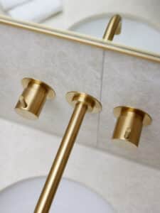 VOLA zeigt die Nahaufnahme einer Waschbecken-Armatur in gold, die in der Wand integriert ist.