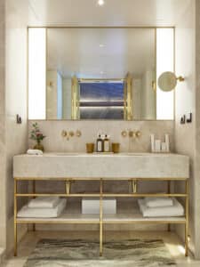 VOLA zeigt ein Marmor-Doppelwaschbecken eines Hotelzimmers mit Armaturen in gold, die in der Wand integriert sind.