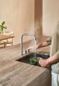 VOLA präsentiert einen Wasserhahn in silber mit zwei Drehreglern, die auf der Arbeitsplatte montiert sind, aus dem kochend heißes Wasser kommt.
