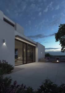 Terrassenbereich einer Flachdach‑Villa bei Nacht mit beleuchteter, eingezogener Markise von Warema.