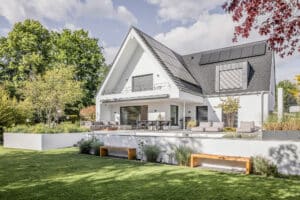 Ein modernes Haus mit einer dachmontierten Solaranlage, überdachtem Balkon, Garten, einer erhöhten Terrasse und silberfarbenen Außenjalousien die mit der Farbe des Dachs harmonieren von Warema.
