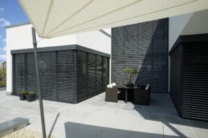 Ein Bungalow mit Eckverglasungen, schwarzen Aussenjalousien und einem Terrassenbereich mit beigem Sonnensegel von Warema.
