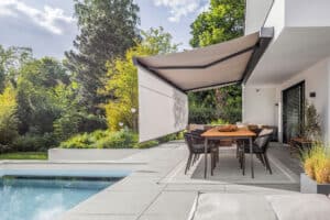 Ein Außenbereich mit Terrasse, Pool, Outdoor‑Möbeln und einer wandmontierten Aussenmarkise mit integrierter Seitenmarkise zur funktionalen Beschattung und Wetterabschirmung von Warema.