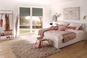 Warema zeigt ein Schlafzimmer mit Terrassentüre in den Garten, die mit Rolläden beschattet werden.