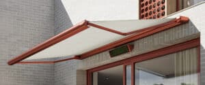 Detailaufnahme einer rotgerahmten Markise aus weissem Stoff - passend zu den roten Fenster, Türrahmen und Fassadenelementen der Villa - von Warema.