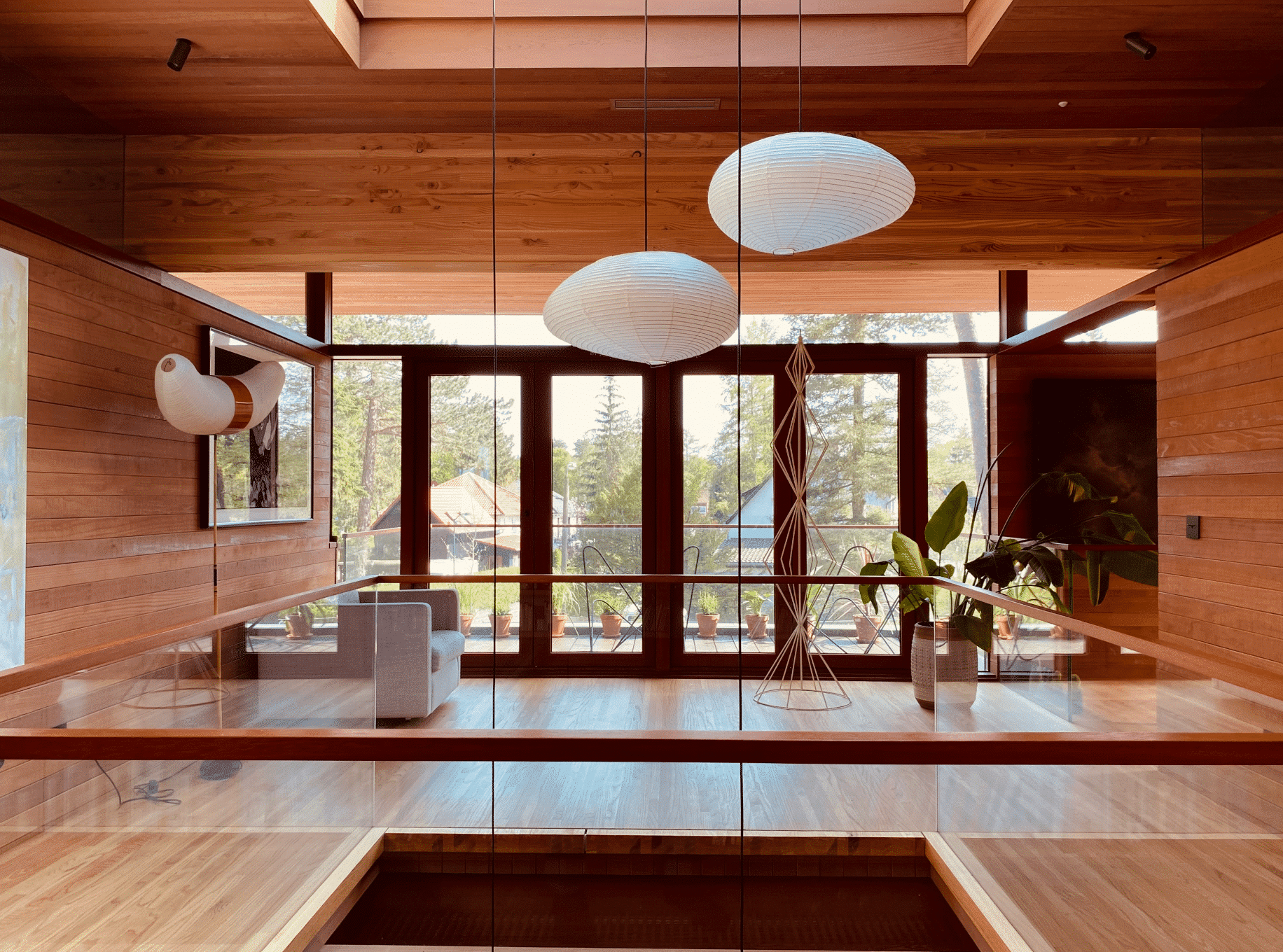 Weissenseer Holz-System-Bau zeigt den Innenbereich eine modernen Holzhauses mit einer Galerie und gläsernem Geländer, einer weissen Hängelampe und Skulpturen.