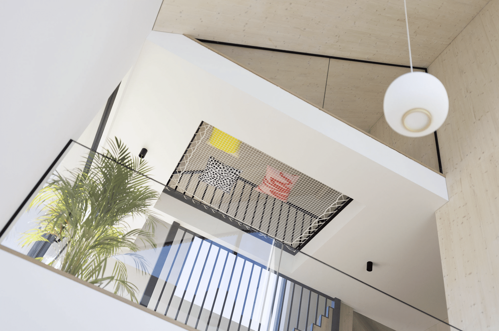 Weissenseer Holz-System-Bau zeigt offenen Wohnraum mit Galerie und Glasgeländer, Stiegenaufgang mit Metallgeländer in den zweiten Stock mit eingearbeitetem Liegenetz im Fußboden.