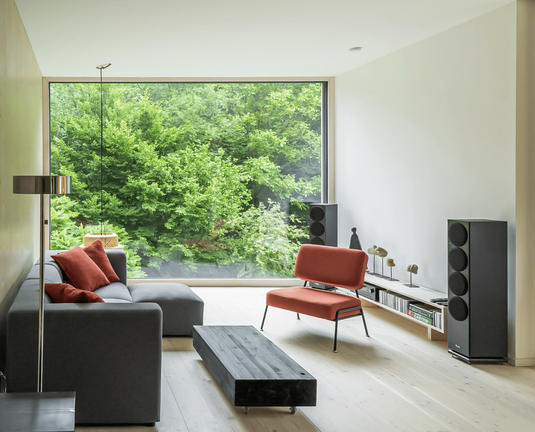 Weissenseer Holz-System-Bau zeigt Wohnzimmer mit Holzboden, dunkler Couch und bodentiefer vollverglaster Front.