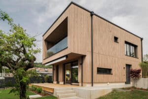 Ein modernes Einfamilienhaus mit Flachdach, Holzfassade, Terrasse, Markise und Balkon von Weissenseer.