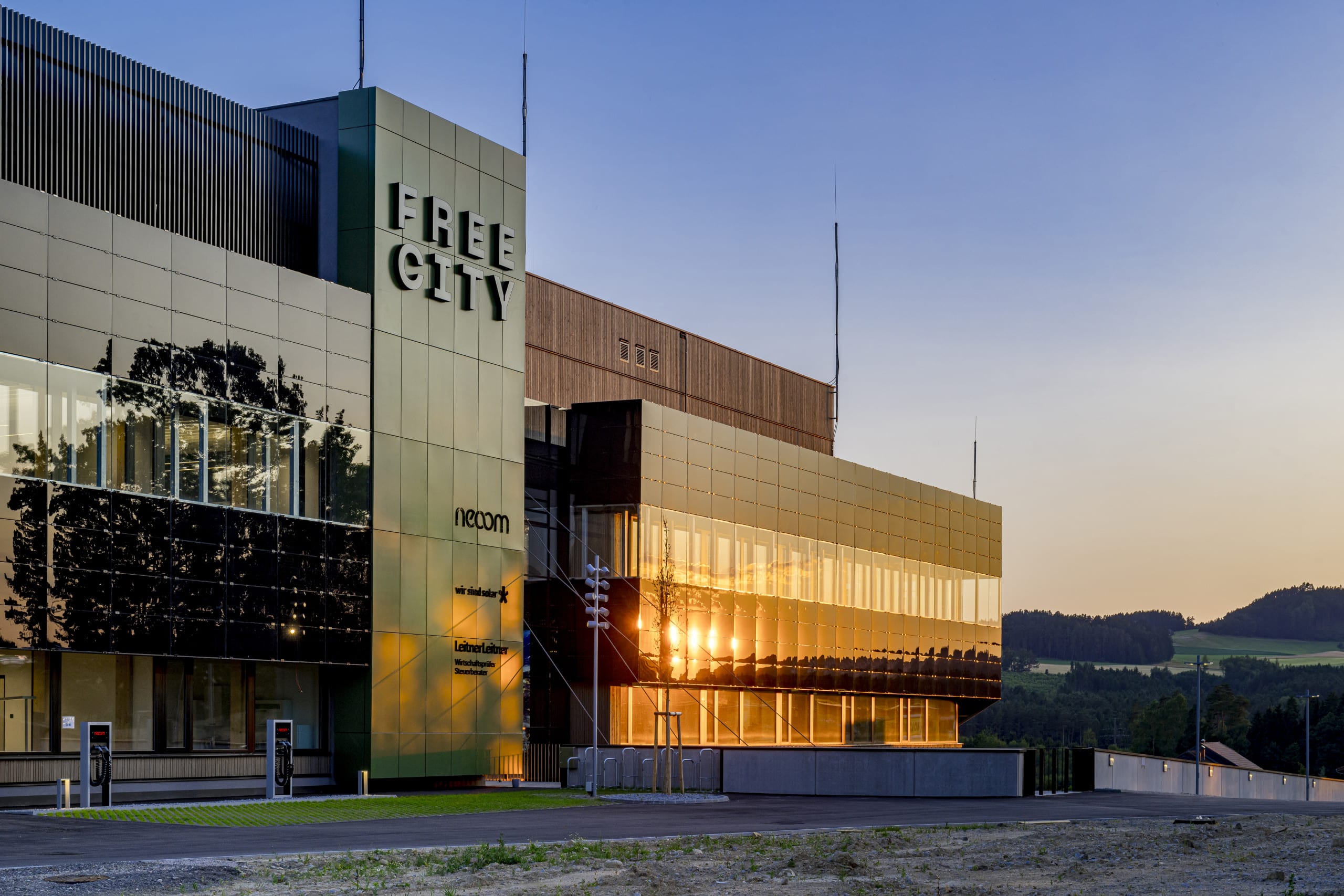 Weissenseer Holz-System-Bau zeigt den Haupteingang das Gebäude der Free City und deren Parkplatz mit Ladestationen.