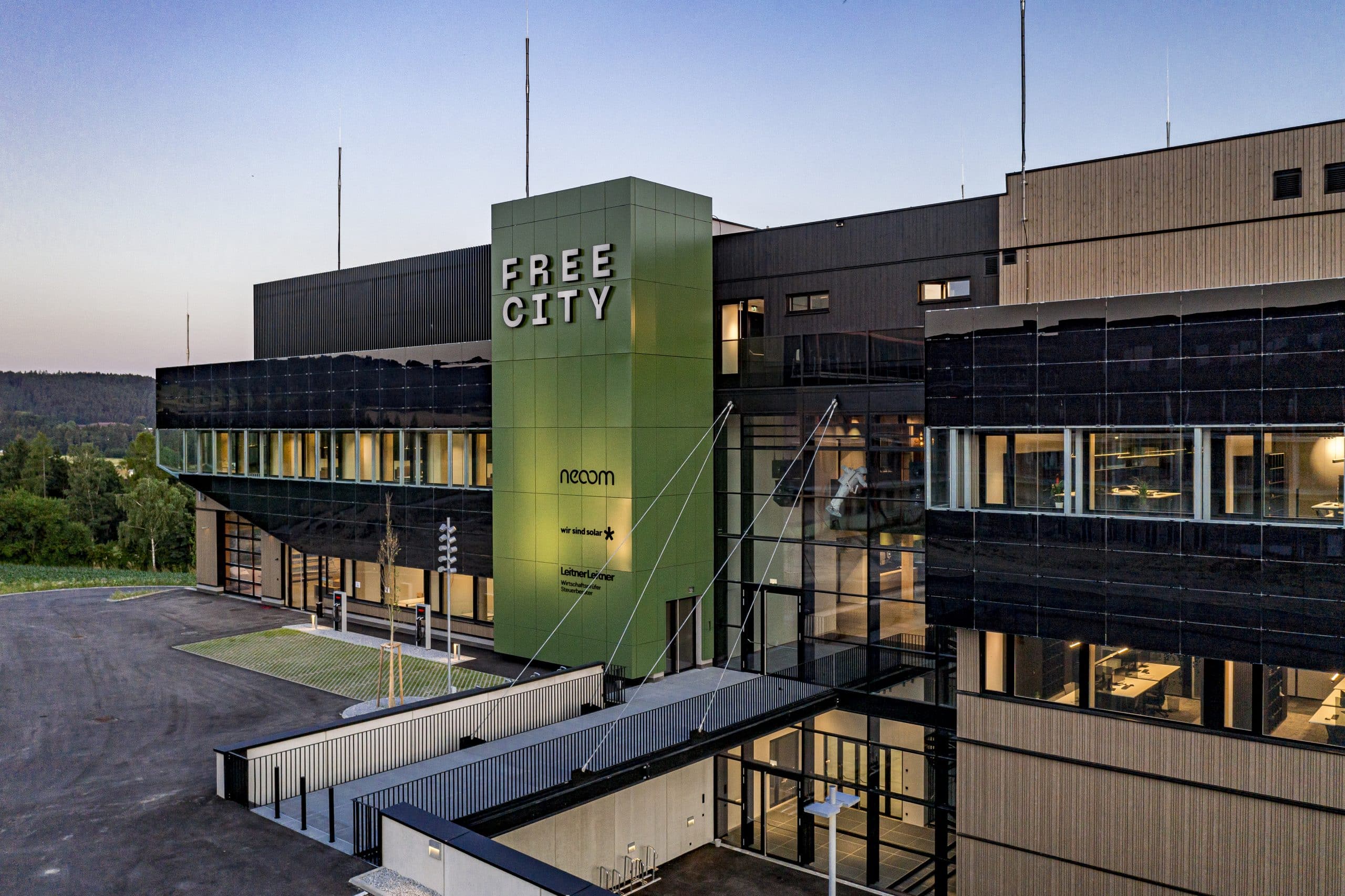 Weissenseer Holz-System-Bau zeigt den Haupteingang das Gebäude der Free City und deren Parkplatz mit Ladestationen.