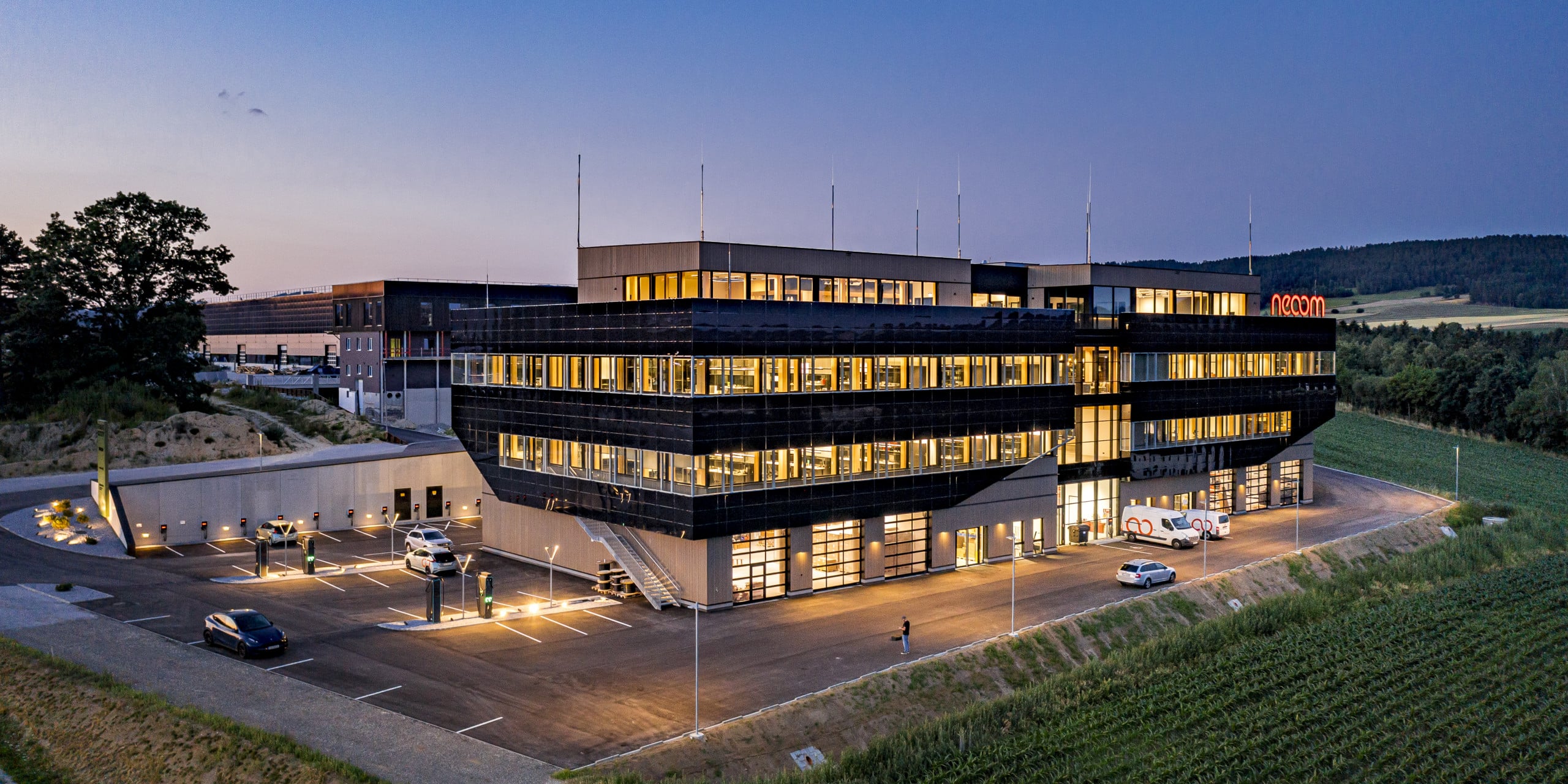 Weissenseer Holz-System-Bau zeigt das Gebäude der Free City und deren Parkplatz mit Ladestationen beleuchtet bei Nacht.