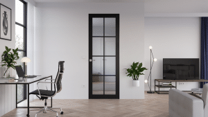 Wohnzimmer mit Arbeitsbereich und einer Innenraumtür aus Glas in Überlänge mit breitem mattschwarzem Rahmen, Mittel- und Quersprossen und kunstvoll gefertigter Türklinke in Silber von WIENTÜR91.