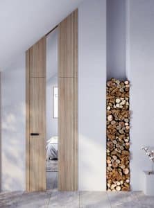 Schlafzimmer mit Fliesenboden, Dachschräge, gemauertem Holzlager und einer Eichentüre mit mattschwarzer Türklinke und einem Spiegelelement in der Türmitte welches in dem dachschrägenangepassten Zargenquerteil weitergeführt wird von WIENTÜR91.