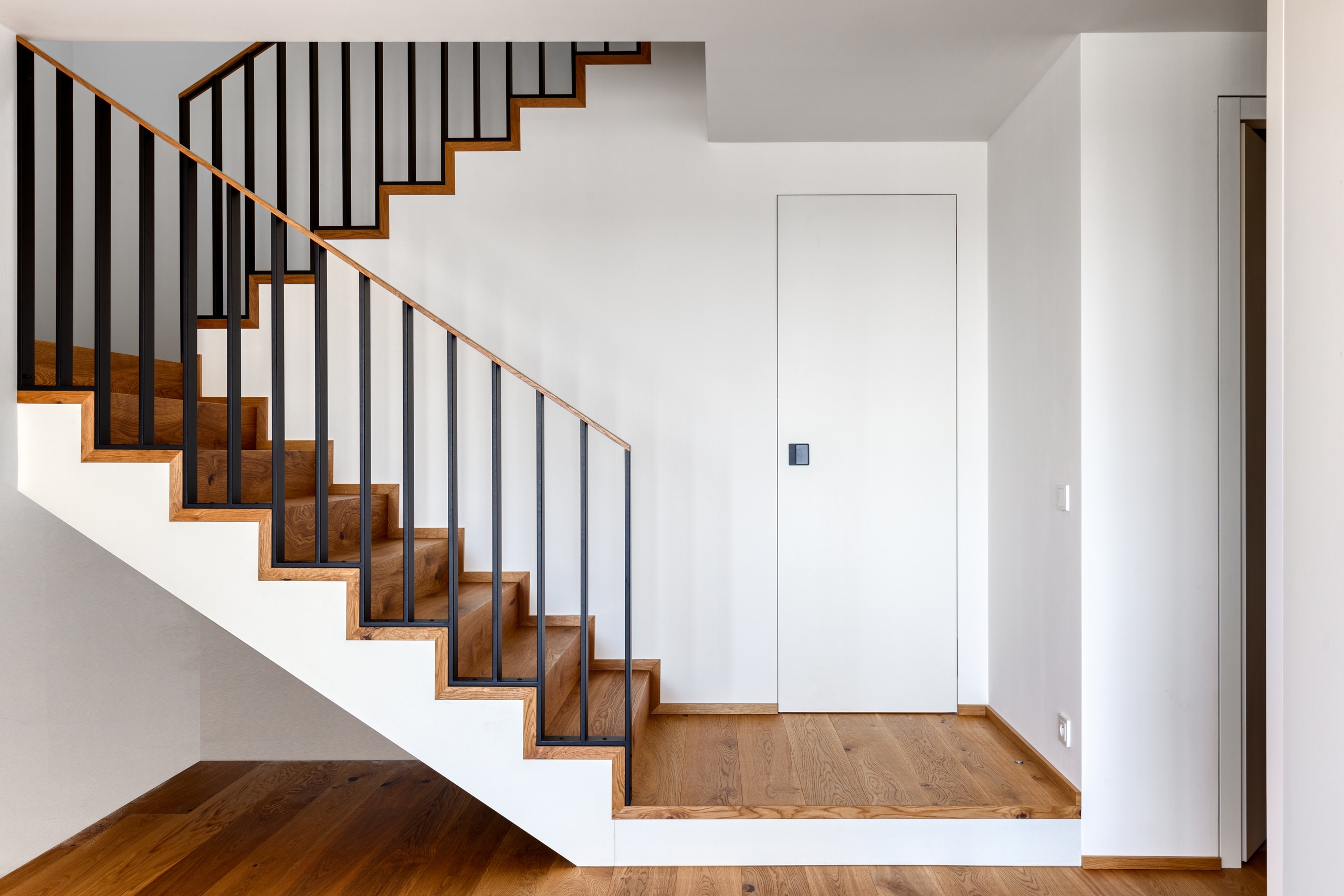 Treppenaufgang mit Plattform und einer zargenlosen weissen Türe mit schwarzem Einlassgriff die zu einer Abstellkammer führt von WIENTÜR91.