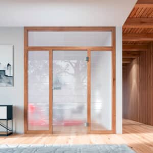 Ein weitläufiger Raum mit einem abgetrennten Zimmer mit Glastrennwand FUTRA, bestehend aus einer Holzrahmung, Glastür, Seitenlichtern und Oberlichte aus satiniertem Glas mit horizontalen Linien von Wientür91.