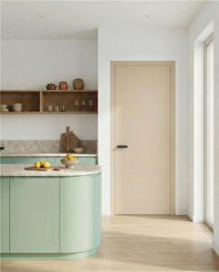 Ein modernes Innentürblatt mit beiger Oberfläche aus Holunderholz mit mattschwarzem minimalistischem Griff ausgestattet, platziert in einer zeitgenössischen Küche mit hellgrünen Fronten, grauer Steinarbeitsplatte und zurückhaltender, warmer Innenraumgestaltung von WIENTÜR91.