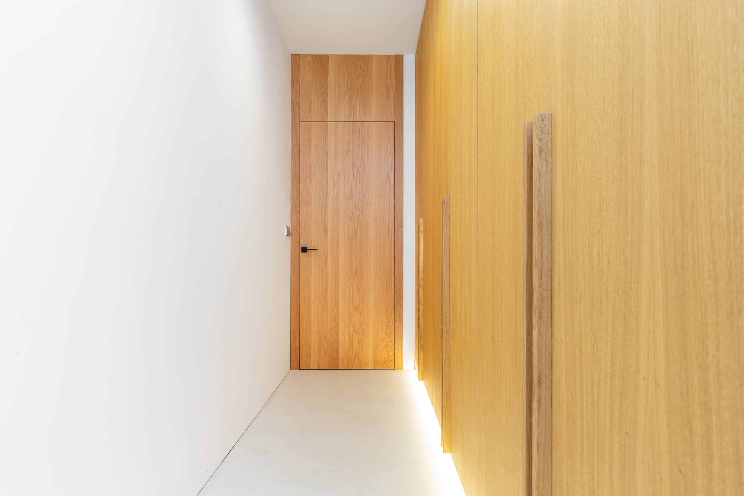 Die moderne deckenbündige Innentür "Rumburk" mit Holzfurnier fügt sich nahtlos in den Vorraum mit passendem Wandverbau ein und schafft ein minimalistisches, elegantes Raumkonzept mit klaren Linien von WIENTÜR91.